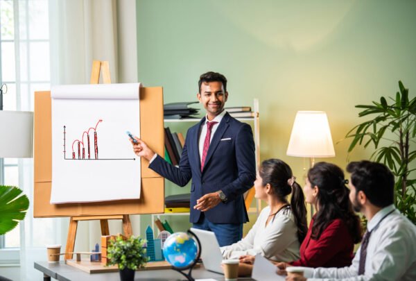 Confident Indian asian male or female boss or trainer make whiteboard presentation at team office meeting