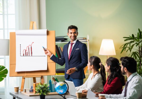 Confident Indian asian male or female boss or trainer make whiteboard presentation at team office meeting
