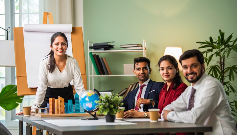 Asian Indian leader in 30s coaching interested business people, giving educational workshop presentation in office. Concentrated employees listening to professional coach at workshop.