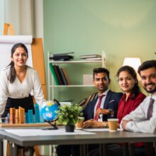 Asian Indian leader in 30s coaching interested business people, giving educational workshop presentation in office. Concentrated employees listening to professional coach at workshop.