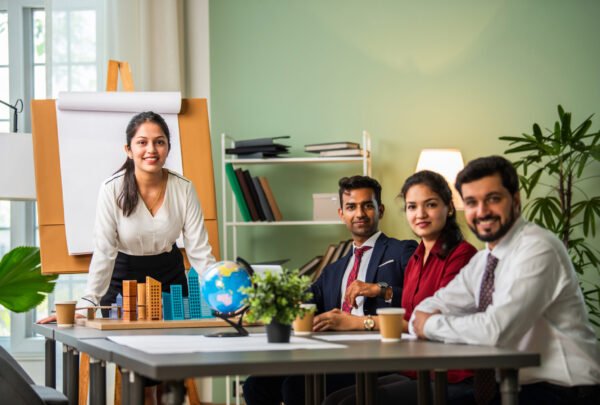 Asian Indian leader in 30s coaching interested business people, giving educational workshop presentation in office. Concentrated employees listening to professional coach at workshop.