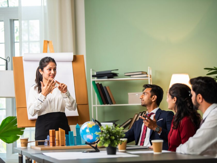 Confident Indian asian male or female boss or trainer make whiteboard presentation at team office meeting