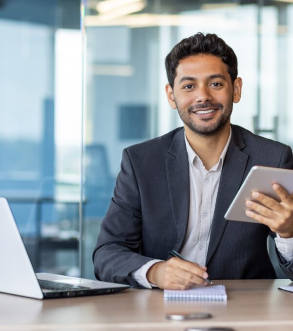Portrait of young businessman with tablet computer inside office, hispanic man smiling and looking at camera, working with laptop, using app on tablet.